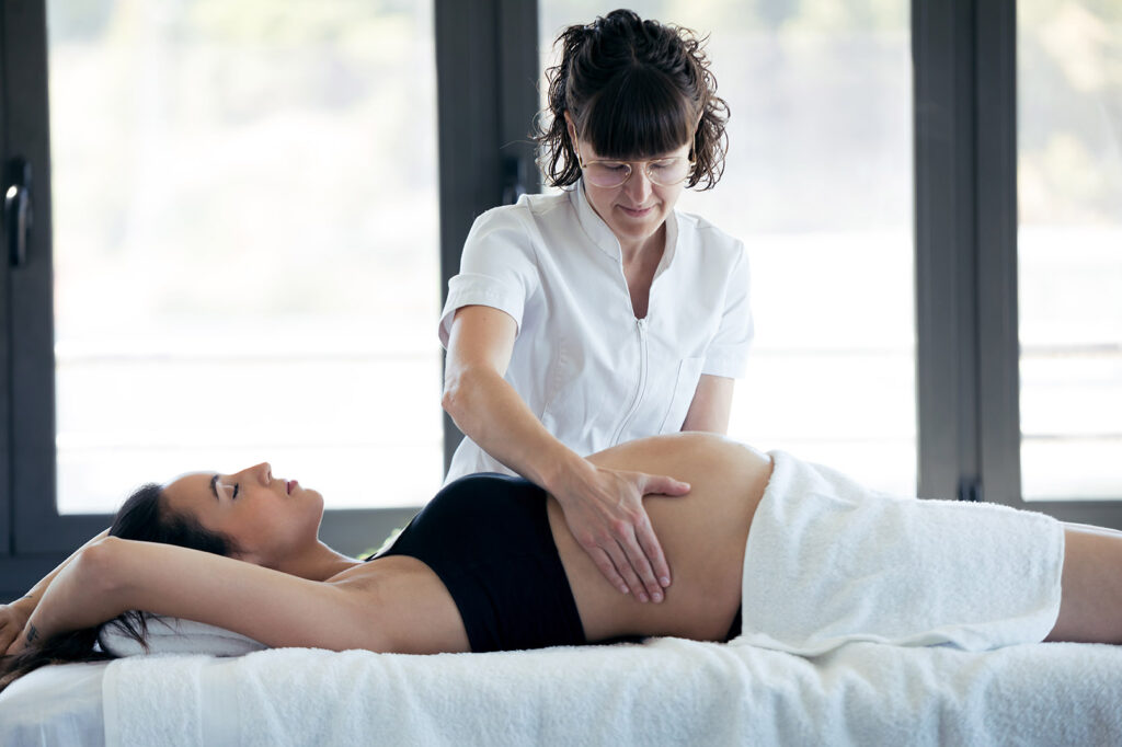 Shot of female physiotherapist massaging tummy on pregnant woman in spa center.